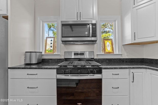 kitchen featuring stainless steel appliances, a wealth of natural light, white cabinets, and dark stone counters