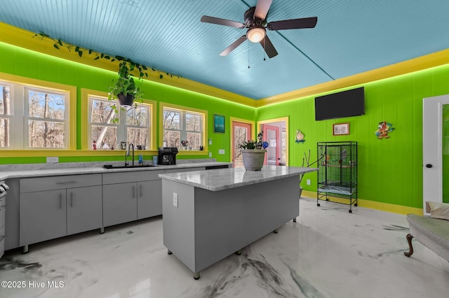 kitchen featuring a kitchen island, a sink, a ceiling fan, and baseboards