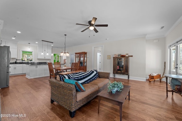 living area with light wood finished floors, baseboards, visible vents, crown molding, and ceiling fan with notable chandelier