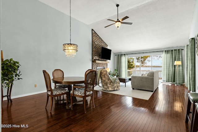 dining area featuring baseboards, high vaulted ceiling, a fireplace, hardwood / wood-style flooring, and ceiling fan with notable chandelier