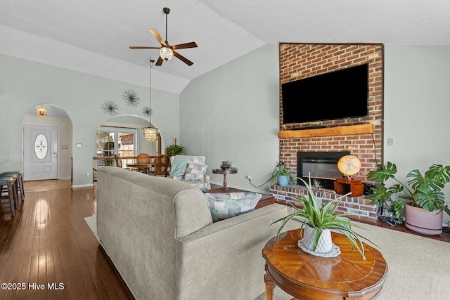 living area featuring baseboards, ceiling fan, lofted ceiling, a fireplace, and hardwood / wood-style flooring