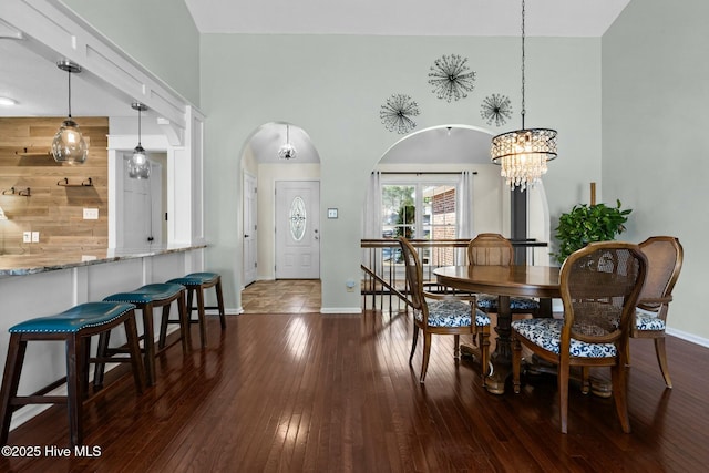 dining space featuring dark wood-type flooring, a notable chandelier, baseboards, and a towering ceiling