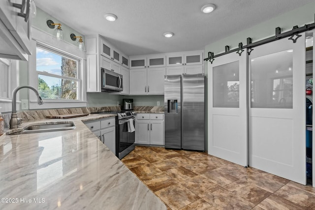 kitchen featuring glass insert cabinets, light stone countertops, a barn door, stainless steel appliances, and a sink