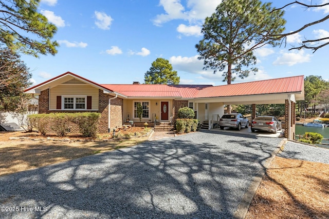 ranch-style house with brick siding, gravel driveway, metal roof, a carport, and a chimney