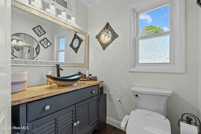 bathroom featuring baseboards, toilet, ornamental molding, wood finished floors, and vanity