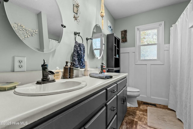 bathroom with visible vents, a wainscoted wall, toilet, a decorative wall, and vanity