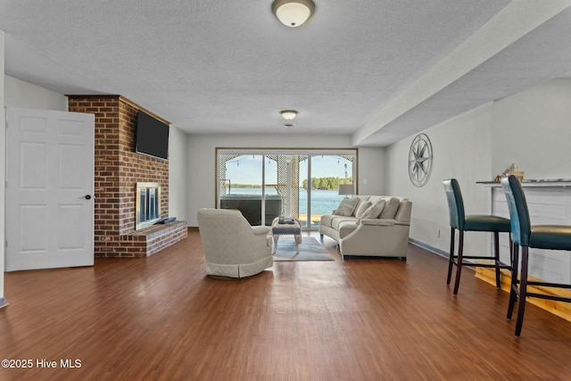 living area featuring baseboards, a textured ceiling, wood finished floors, and a fireplace