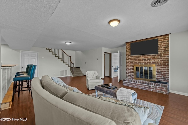 living area featuring visible vents, a brick fireplace, wood finished floors, and stairway