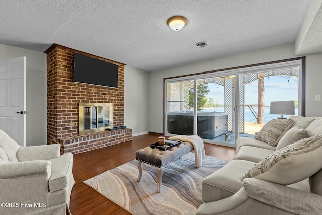 living area featuring visible vents, a textured ceiling, a brick fireplace, and wood finished floors