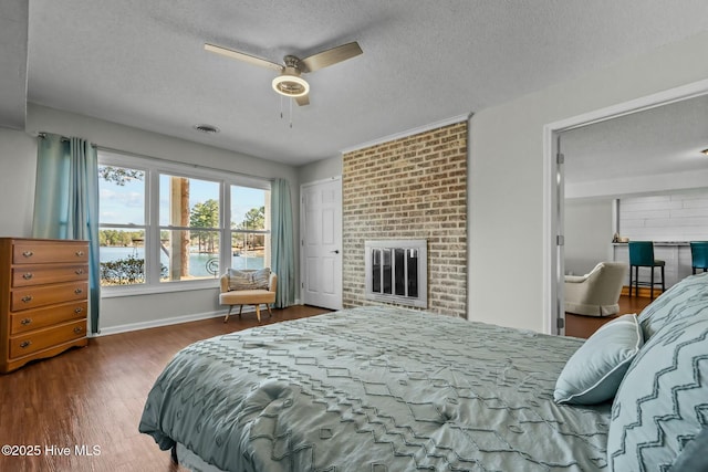 bedroom featuring wood finished floors, baseboards, visible vents, a textured ceiling, and a brick fireplace