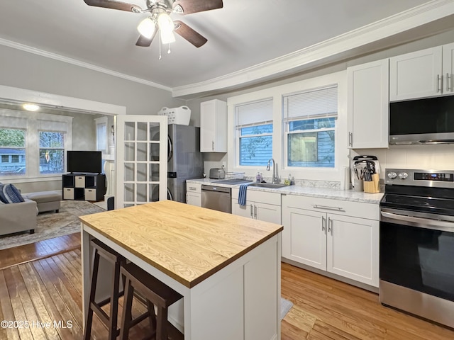 kitchen with a sink, stainless steel appliances, light wood-style floors, and ornamental molding