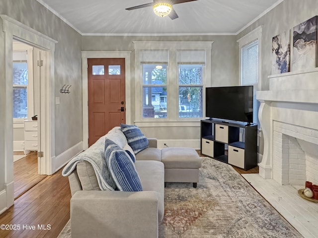 living area with crown molding, a brick fireplace, baseboards, and wood-type flooring