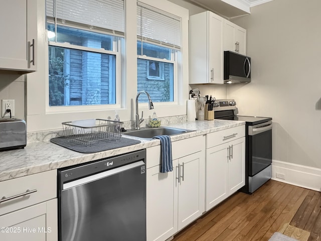 kitchen with a sink, white cabinetry, stainless steel appliances, light countertops, and dark wood-style flooring