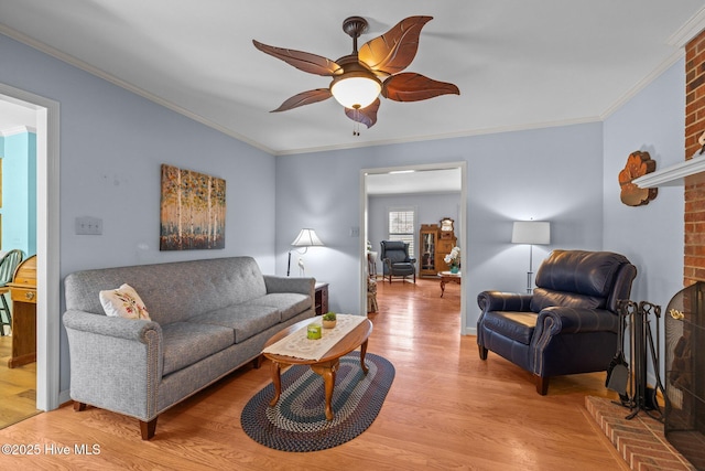 living room with ceiling fan, a brick fireplace, light wood-style flooring, and crown molding