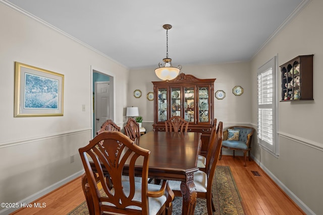 dining area with light wood-type flooring, baseboards, visible vents, and crown molding