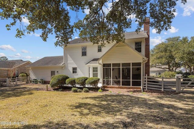 back of property featuring a sunroom, a chimney, fence, and a lawn