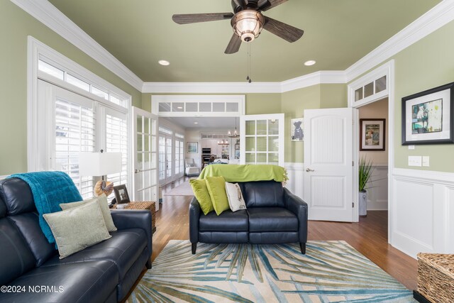 living area with a ceiling fan, a wainscoted wall, ornamental molding, and wood finished floors