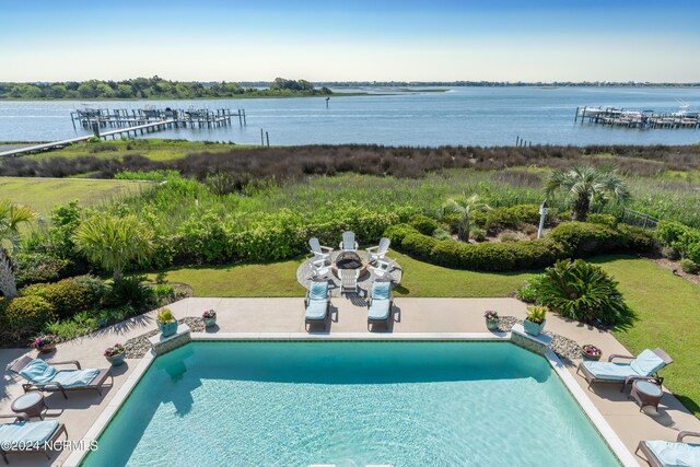 view of swimming pool featuring fence, a water view, a pool with connected hot tub, a fire pit, and a patio area