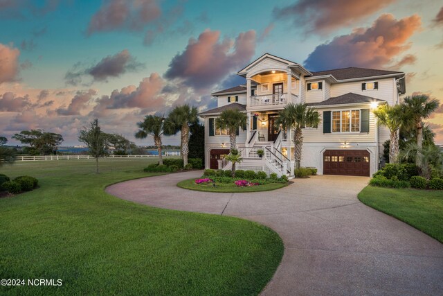 beach home featuring a balcony, curved driveway, an attached garage, and a yard