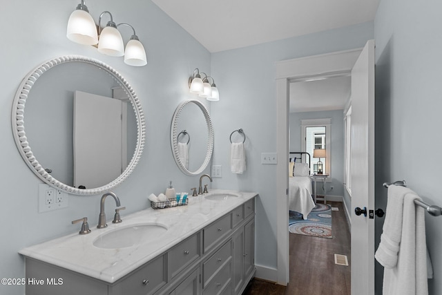 ensuite bathroom with double vanity, wood finished floors, baseboards, and a sink