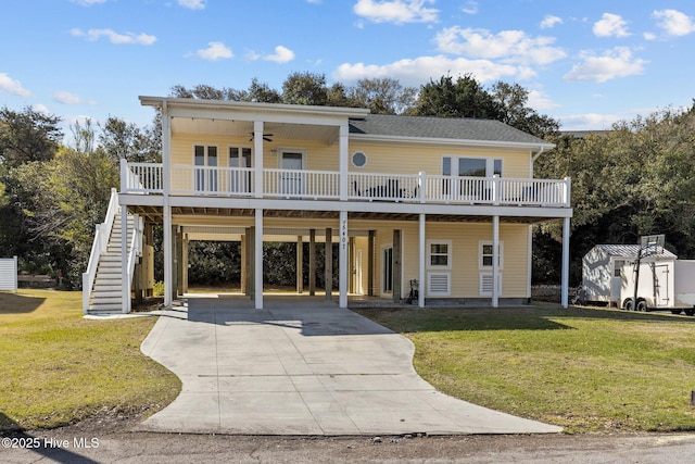 coastal home featuring a front lawn, concrete driveway, stairs, and ceiling fan