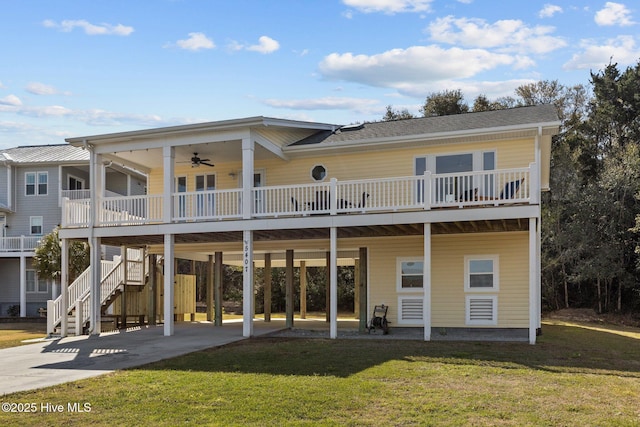 rear view of property with a lawn, a ceiling fan, concrete driveway, a carport, and stairs