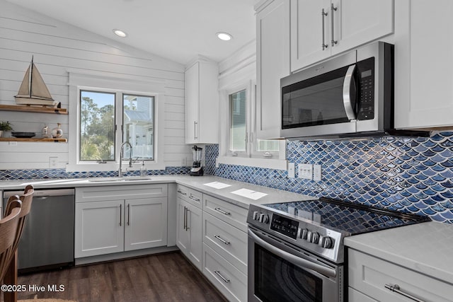 kitchen with dark wood finished floors, lofted ceiling, a sink, light countertops, and appliances with stainless steel finishes