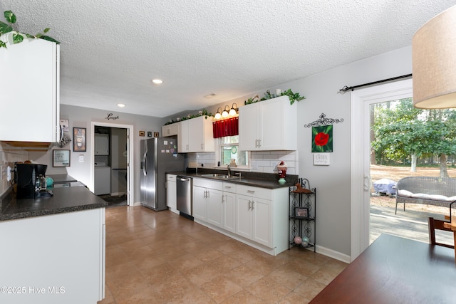 kitchen with appliances with stainless steel finishes, dark countertops, a sink, and washer / dryer