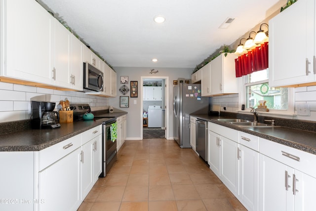 kitchen featuring dark countertops, appliances with stainless steel finishes, washer / clothes dryer, white cabinetry, and a sink