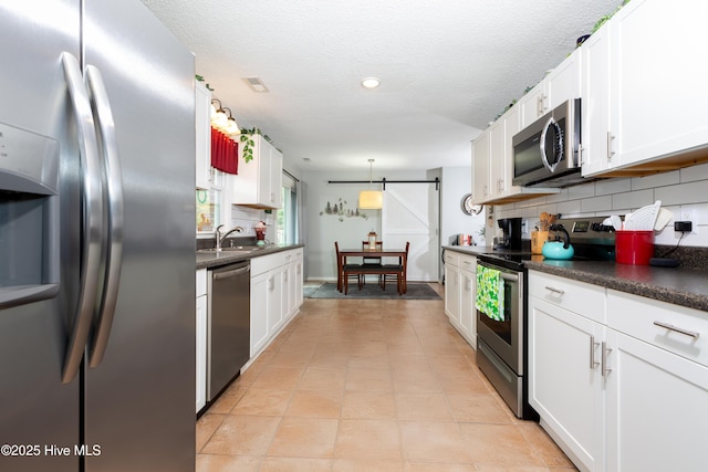 kitchen featuring dark countertops, a barn door, stainless steel appliances, and decorative backsplash