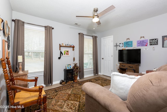 living area with visible vents, a wood stove, ceiling fan, a textured ceiling, and baseboards