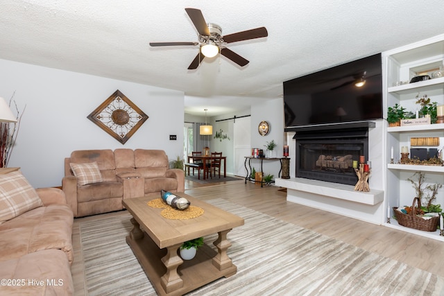 living area with built in shelves, a barn door, ceiling fan, a textured ceiling, and wood finished floors