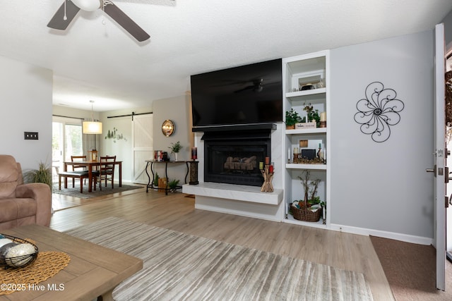 living room featuring baseboards, a barn door, a ceiling fan, and wood finished floors