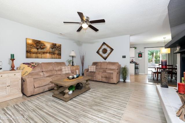 living area featuring light wood-type flooring, ceiling fan, visible vents, and a textured ceiling