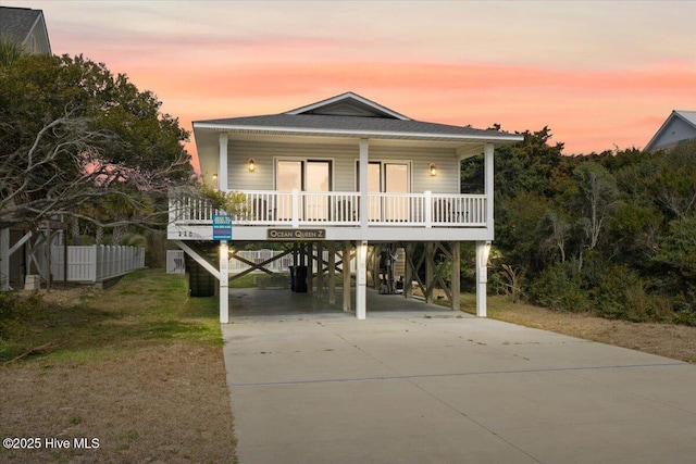 raised beach house featuring a carport, a porch, a front yard, and driveway