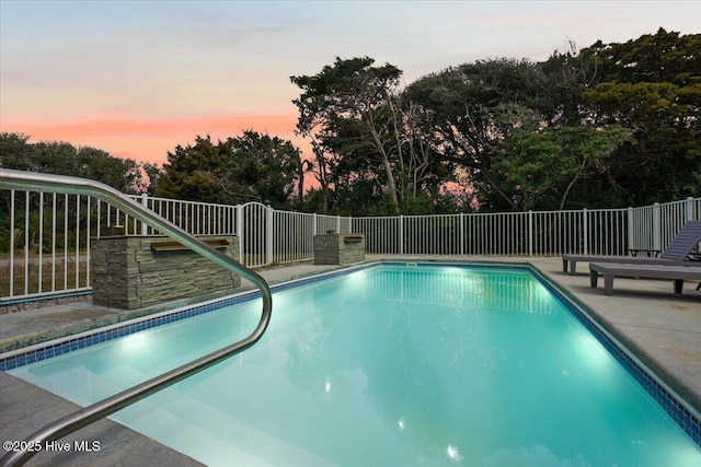 220 W Dolphin Dr, Oak Island, NC 28465 - pool at dusk with fence, view of scattered trees, and a patio area