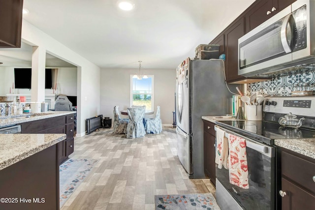 kitchen featuring dark brown cabinetry, light stone counters, stainless steel appliances, and light wood-style floors