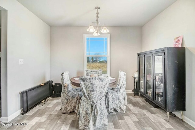 dining room with light wood-type flooring, a notable chandelier, and baseboards