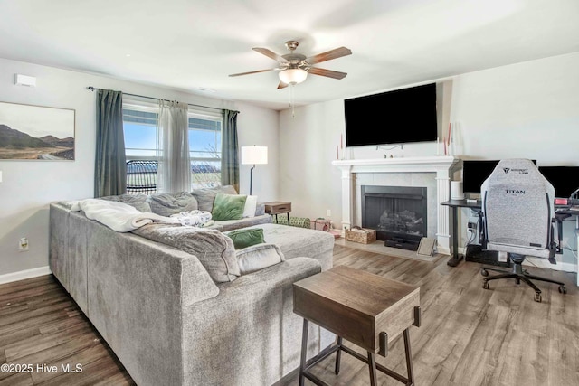 living area featuring a ceiling fan, a tiled fireplace, baseboards, and wood finished floors