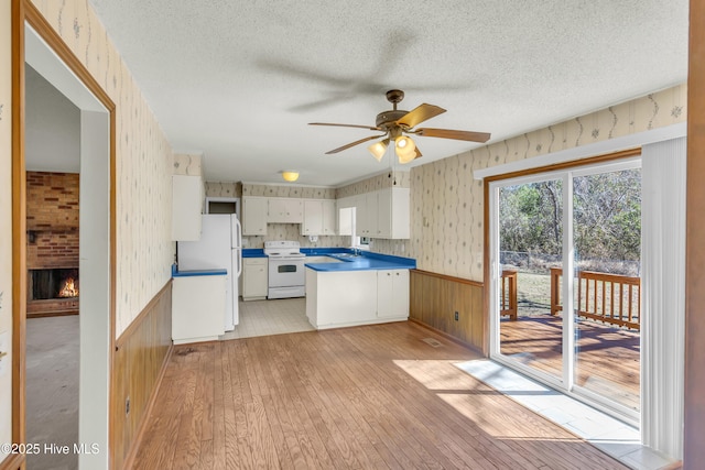 kitchen featuring a textured ceiling, a peninsula, white appliances, wainscoting, and wallpapered walls