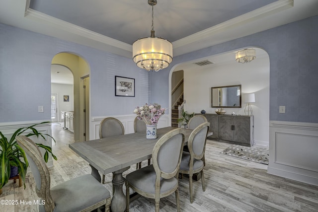 dining space with arched walkways, a raised ceiling, visible vents, wainscoting, and wood finished floors