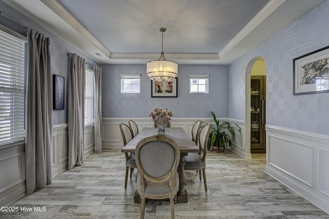 dining space featuring light wood-style floors, a tray ceiling, a wainscoted wall, and arched walkways