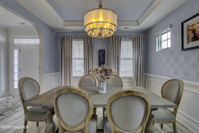 dining space with a raised ceiling, wood finished floors, and wainscoting