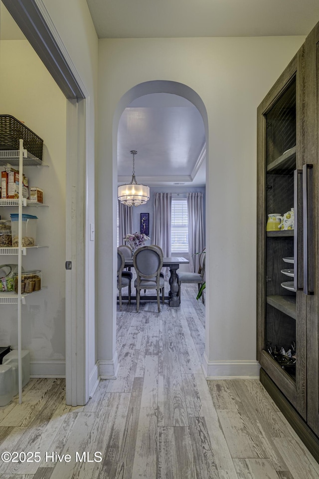 hallway with arched walkways, wood finished floors, and a chandelier