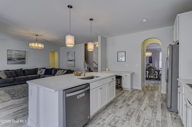 kitchen featuring arched walkways, stainless steel appliances, light wood-style floors, white cabinets, and a sink