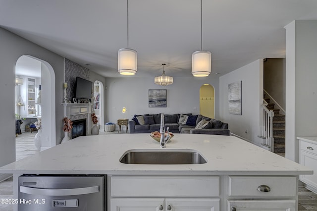 kitchen featuring stainless steel dishwasher, open floor plan, a large fireplace, a sink, and light stone countertops