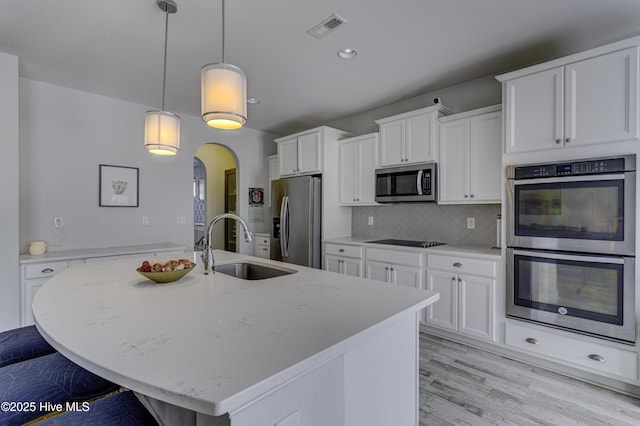 kitchen featuring visible vents, arched walkways, appliances with stainless steel finishes, white cabinetry, and a sink