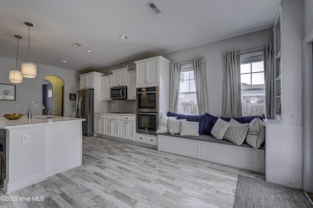 kitchen with arched walkways, stainless steel appliances, a sink, visible vents, and white cabinetry