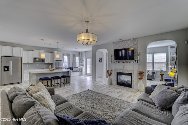 living room featuring arched walkways, light wood-style flooring, a notable chandelier, a large fireplace, and recessed lighting