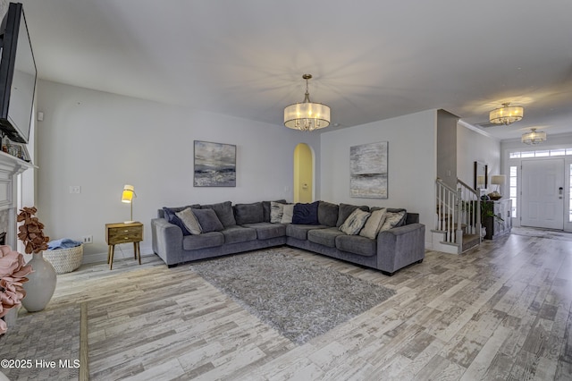 living area featuring arched walkways, a fireplace, a notable chandelier, light wood-style flooring, and stairway